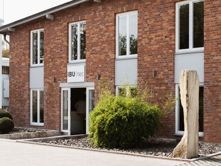 Das Firmengebäude der IBUTec mit einer braun-roten Backstein-Fassade und weißen Fenstern.
