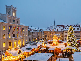 Weimarer Weihnacht Rathaus Ein festlich beleuchteter Weihnachtsmarkt mit schneebedeckten Ständen und einem großen, geschmückten Weihnachtsbaum in der Mitte.