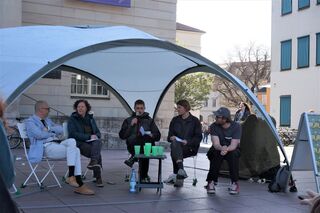 5 Menschen auf Stühlen unter einem Pavillon diskutieren