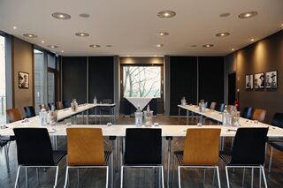 Moderne Konferenzräume mit eleganter Einrichtung und natürlichem Licht Ein moderner Konferenzraum mit einem langen Tisch, umgeben von Stühlen, und einem großen Fenster, das Tageslicht hereinlässt.