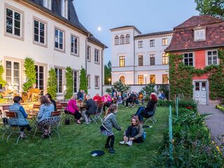 Lange Nacht der Museen in Goethes Hausgarten Zwei Mädchen spielen im Gras, während Erwachsene an Tischen sitzen und sich unterhalten, während die Dämmerung einsetzt.