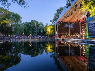 Konzertnacht Bella Italia Ein wunderschöner Abend mit einer gut beleuchteten Seebühne im Weimarhallenpark, auf der Musiker spielen, während das Publikum in der Natur entspannt.