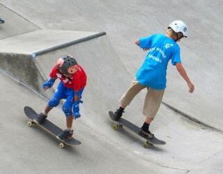 Jugendliche fahren auf Skateboards eine Skateboard-Rampe herab.