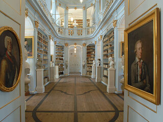 Zwei Porträts in goldenen Rahmen hängen an den Wänden, während das Licht sanft durch den Raum strömt.