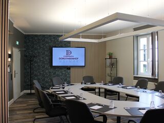 Moderne Konferenzraumgestaltung im Dorotheenhof Weimar Ein moderner Konferenzraum mit einem großen Tisch, Stühlen und einem Bildschirm, der das Logo des Dorotheenhofs Weimar zeigt.