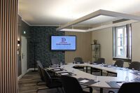 Ein moderner Konferenzraum mit einem großen Tisch, Stühlen und einem Bildschirm, der das Logo des Dorotheenhofs Weimar zeigt.