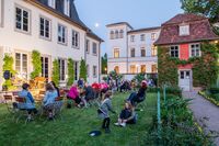 Zwei Mädchen spielen im Gras, während Erwachsene an Tischen sitzen und sich unterhalten, während die Dämmerung einsetzt.