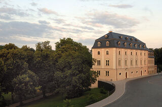 Anna Amalia Bibliothek Ein elegantes, mehrstöckiges Gebäude mit einem blauen Dach, umgeben von üppigem Grün und einem sanften Weg im Vordergrund.