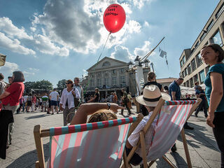 Auf dem Theaterplatz sind viele Menschen versammelt, einige genießen das Fest, während ein roter Ballon über ihnen schwebt.