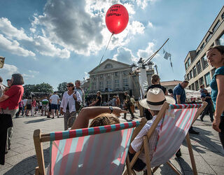 Auf dem Theaterplatz sind viele Menschen versammelt, einige genießen das Fest, während ein roter Ballon über ihnen schwebt.