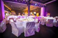 Elegante Tische mit weißen Tischdecken und Kerzenleuchtern schaffen eine festliche Atmosphäre in einem modernen Veranstaltungsraum.