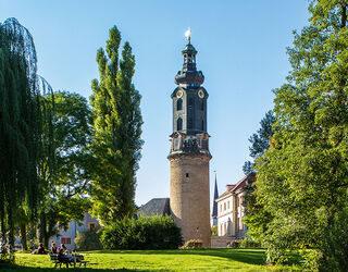 Stadtschloss Im Vordergrund sitzen Menschen auf einer Bank, während der markante Turm im Hintergrund die Szenerie dominiert und Ruhe ausstrahlt.