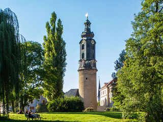 Stadtschloss Im Vordergrund sitzen Menschen auf einer Bank, während der markante Turm im Hintergrund die Szenerie dominiert und Ruhe ausstrahlt.