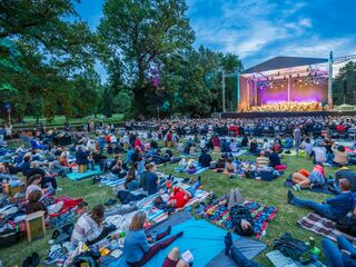 Open-Air Konzert mit begeistertem Publikum im Park Familien und Freunde versammeln sich auf bunten Decken, während sie die Musik eines Orchesters im Freien erleben.