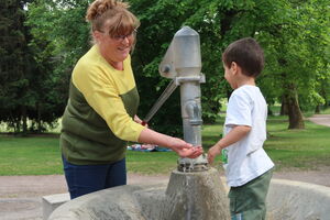 Familienpatin Frau Wenzel mit Hannes an einem Brunnen