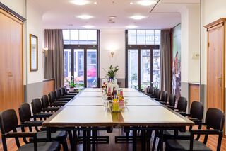 Tafelrunde Hotel Anna Amalia Ein eleganter Besprechungsraum mit einem langen Tisch, umgeben von schwarzen Stühlen und dekorativen Pflanzen im Hintergrund.