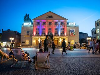 Kunstfest Weimar auf dem Theaterplatz Weimar Der Theaterplatz ist voller Leben, mit Besuchern, die sich um ein kunstvoll beleuchtete Deutsche Nationaltheater Weimar und Liegestühle versammeln.