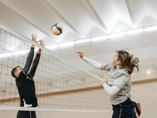 Symbolbild: Ein Mann und eine Frau spielen Volleyball, sie befinden sich im Sprung beim Schlagabtausch