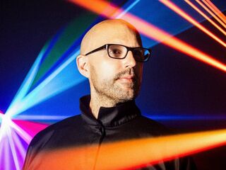 Ein Mann im Fokus mit bunten Lichtstrahlen im Hintergrund Ein Mann mit Glatze und Brille steht vor einem bunten Lichtspiel aus roten, blauen und grünen Strahlen.