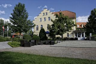 Einladender Gartenbereich vor einem historischen Gebäude Ein elegantes Gebäude mit einem markanten Giebeldach, umgeben von gepflegten Gärten und modernen Sitzgelegenheiten im Freien.