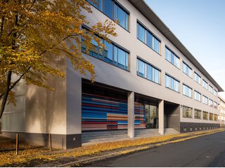 Faszinierende Fassade eines modernen Gebäudes im Herbst Ein modernes Gebäude mit großen Fenstern, umgeben von buntem Herbstlaub, das die Straße säumt.