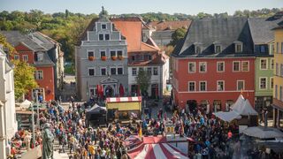 Zwiebelmarkt Eine lebendige Szene mit Menschen, die sich um Marktstände versammeln, während die Sonne auf die bunten Fassaden scheint.