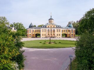 Schloss Belvedere Ein prächtiges Schloss mit gelber Fassade und Kuppeldach, umgeben von üppigem Grün und einem gepflegten Garten.