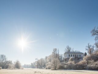 Park an der Ilm Ein strahlender Wintertag mit klarem Himmel, der die gefrorene Landschaft und ein elegantes Gebäude beleuchtet.