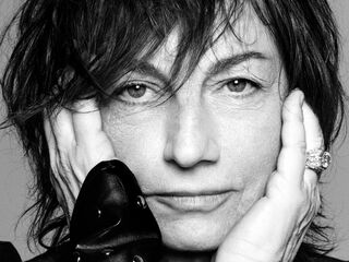 Gianna Nannini mit zerzaustem Haar schaut direkt in die Kamera, ihre Hände stützen ihr Gesicht, was eine nachdenkliche Stimmung erzeugt.