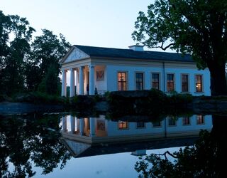 Lange Nacht der Museen Die Fassade eines historischen Hauses mit Säulen und beleuchteten Fenstern steht im Kontrast zur Dämmerung und dem stillen Wasser.