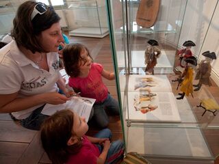 Lange Nacht der Museen Die Kinder sind fasziniert von den Puppen in der Vitrine, während die Mutter ihnen Informationen aus einem Heft vorliest.