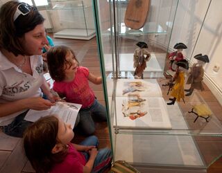 Lange Nacht der Museen Die Kinder sind fasziniert von den Puppen in der Vitrine, während die Mutter ihnen Informationen aus einem Heft vorliest.