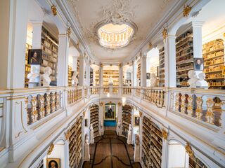 Anna Amalia Bibliothek Der Blick auf eine opulente Bibliothek mit goldenen Verzierungen, hohen Decken und einer zentralen Treppe, die zu weiteren Regalen führt.