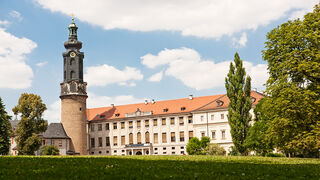 Stadtschloss Ein beeindruckendes Schloss mit einem hohen Turm, das von einem gepflegten Garten und großen Bäumen umgeben ist, unter einem klaren Himmel.