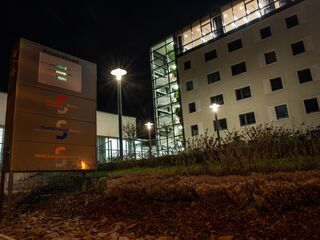 Städtische Energieversorgung: Stadtwerke in Weimar Die Fassade der Stadtwerke mit großen Fenstern, das nachts erleuchtet ist, umgeben von gepflegten Pflanzen und Steinen.