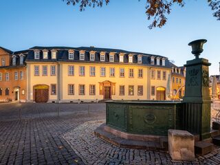 Ein historisches Gebäude mit gelber Fassade und vielen Fenstern, beleuchtet von warmem Licht in der Dämmerung.
