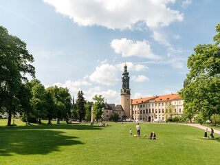 Stadtschloss und Bastille Eine weitläufige Wiese mit Menschen, die sich entspannen, umgeben von Bäumen und dem Weimarer Stadtschlossturm im Hintergrund.