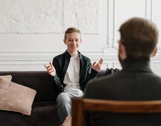 Jugendlicher auf einem Sofa, von hinten sieht man eine erwachsene Person, sie sind in einem Gespräch