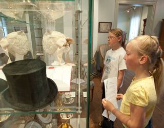Lange Nacht der Museen Die beiden Kinder, eines mit Brille, studieren aufmerksam die Details von antiken Hüten in einer Glasvitrine.
