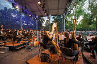 Die Staatskapelle Weimar spielt auf einer großen Bühne im Weimarhallenpark unter Bäumen.
