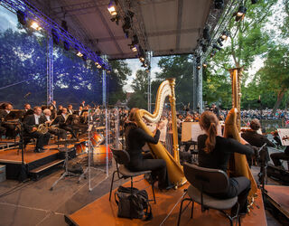 Staatskapelle Weimar Konzertnacht Die Staatskapelle Weimar spielt auf einer großen Bühne im Weimarhallenpark unter Bäumen.