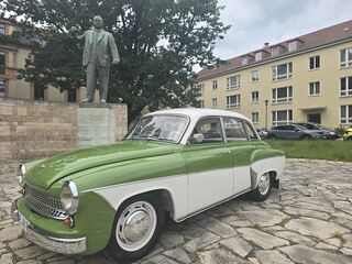 Grüner Oldtimer parkt neben einer Statue eines Politikers Das Bild zeigt ein historisches Auto vor einer Statue, die Ernst Thälmann darstellt, mit einer Mischung aus Natur und urbanem Leben.