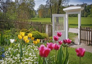 Park an der Ilm, Goethes Gartenhaus, Foto: Matthias Eckert Ein idyllischer Garten mit einer weißen Tür, umgeben von blühenden Blumen und einer weitläufigen, grünen Wiese im Hintergrund.