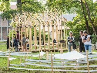 summaery an der Bauhaus-Universitaet Weimar Eine Gruppe von Menschen steht in einem Park und betrachtet eine kreative Holzstruktur, umgeben von grünen Bäumen.
