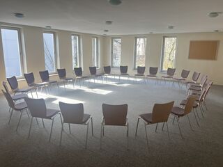 Hummelhaus Weimar Seminarraum Ein heller Raum mit großen Fenstern, in dem Stühle im Kreis angeordnet sind, bereit für eine Gruppensitzung oder Diskussion.