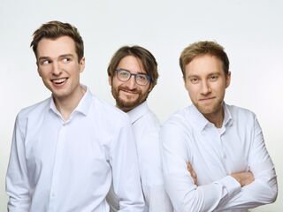 Weimarer Kabarett Drei Männer in weißen Hemden stehen in einer Reihe, lächeln und zeigen unterschiedliche Gesichtsausdrücke.