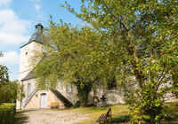 Eine Kirche in Mellingen mit einem markanten Turm, umgeben von üppigem Grün und einem klaren blauen Himmel.
