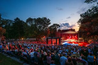 Eine große Menschenmenge versammelt sich beim Meute-Konzert im Weimarhallenpark, während die Sonne hinter den Bäumen untergeht.