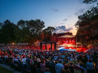 Eine große Menschenmenge versammelt sich beim Meute-Konzert im Weimarhallenpark, während die Sonne hinter den Bäumen untergeht.