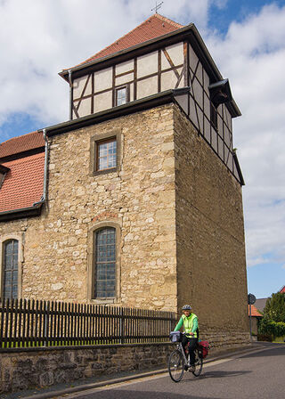 Die charmante Steinkirche mit Fachwerk und roten Dächern wird von einem Radfahrer auf der Straße flankiert.